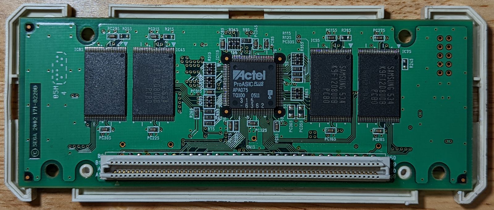 Photo of Triforce Type 3 NAND cartridge interior, bottom view. Four more Samsung 64M flash memory chips are visible on the bottom, as well as an ASIC chip labeled 'Actel ProASIC Plus', and the 120-pin connector below it.