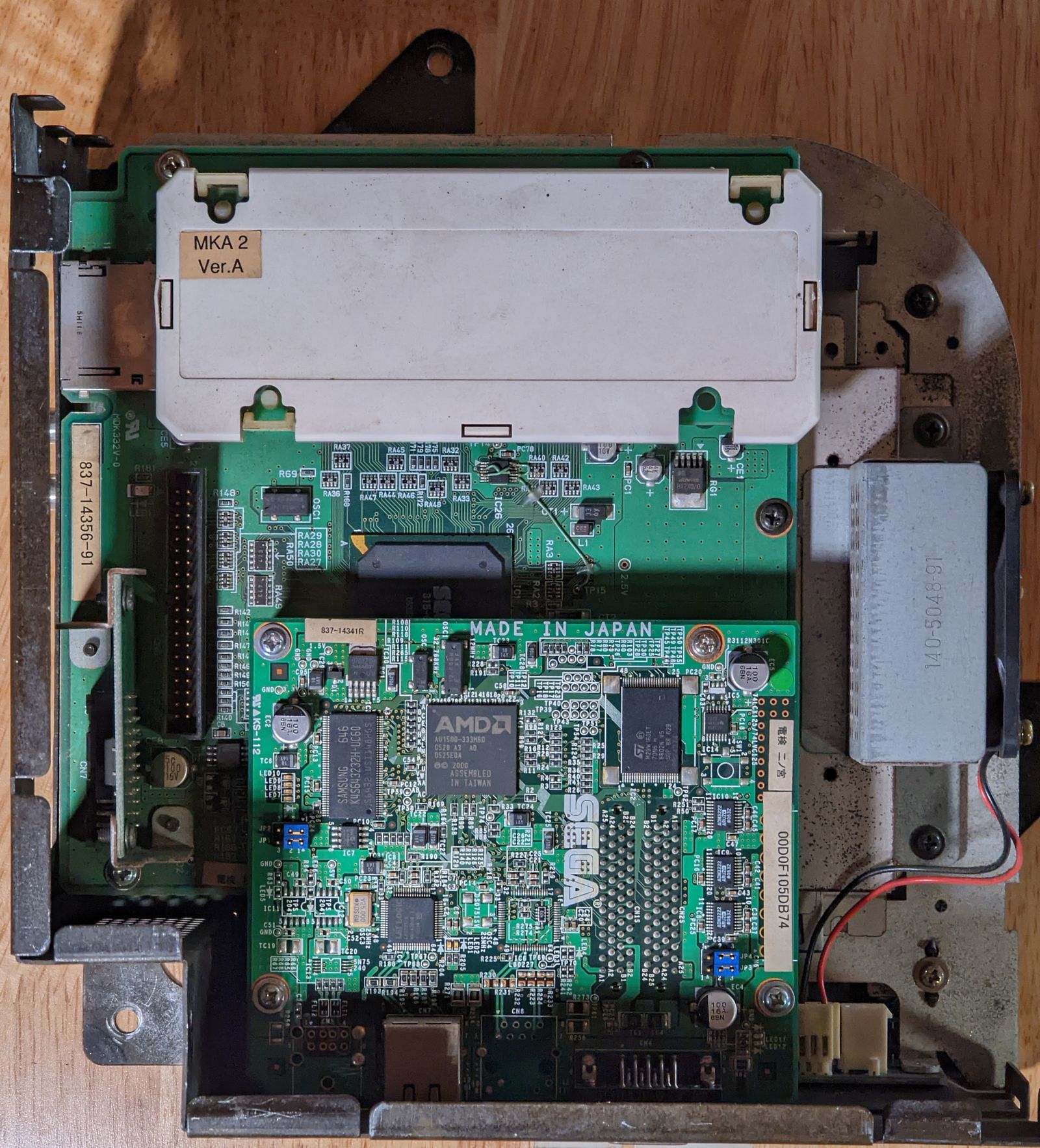 Photo of Triforce Type 3 interior, top view, showing a NAND cartridge, what appears to be a network interface board, and a glimpse of the media board underneath it. The NAND cartridge is labeled MKA 2 Ver.A. There is an AMD Au1500 chip visible on the network interface board.